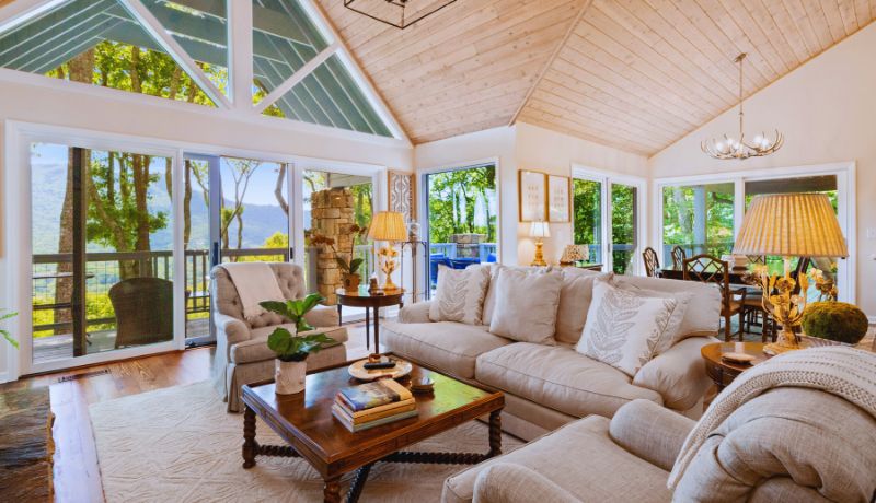 A beautifully decorated and spacious living room with a high, vaulted ceiling made of light-colored wood and filled with natural light coming through large windows and glass doors
